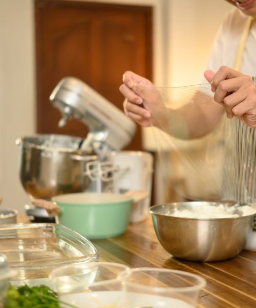 Man covering a mixing bowl of whipped cream with plastic wrap, ready for refrigeration.