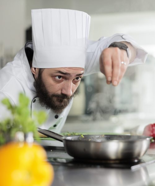 Master cook putting parmesan cheese in food while preparing meal for dinner service at restaurant. Gastronomic expert in professional kitchen seasoning gourmet dish served at fine dining.